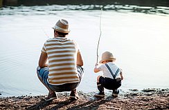 Junger Vater mit seinem kleinen Sohn beim Angeln am See
