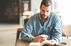 Junger Mann liest an einem Tisch ein Buch