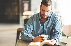 Junger Mann liest an einem Tisch ein Buch