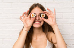 Lachende junge Frau hält sich Sushi-Rollen vor die Augen
