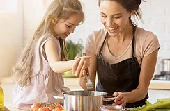 Frau mit Schürze kocht mit ihrer Tochter am Herd