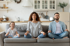 Tochter, Mutter und Vater im Yoga-Sitz auf der Couch
