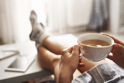 Person mit Füßen auf dem Tisch und Teetasse in der Hand